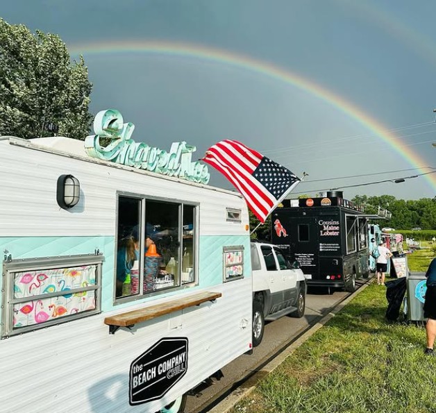 The camper under a full rainbow with an American flag flying